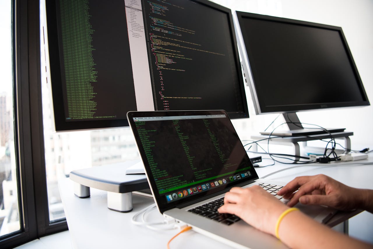gallery-01 A developer writes code on a laptop in front of multiple monitors in an office setting.